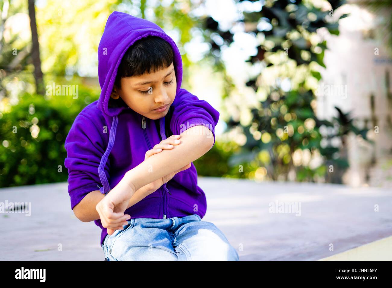 young indian kid itching skin or rashes at park - concept of skincare, allergy, winter infecton and medical Stock Photo