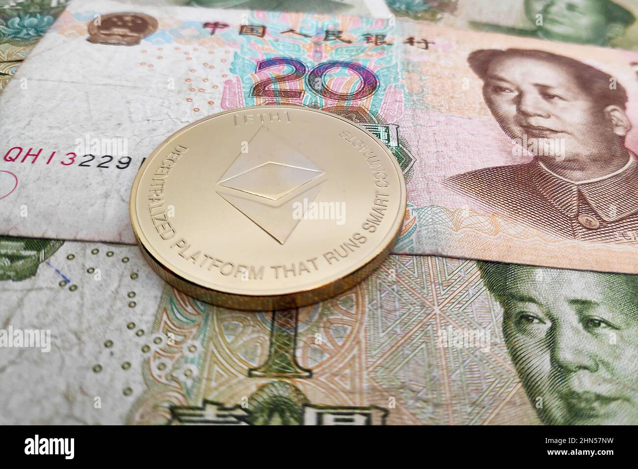 Close-up on a golden Ethereum coin on top of a stack of Chinese Yuan banknotes. Stock Photo