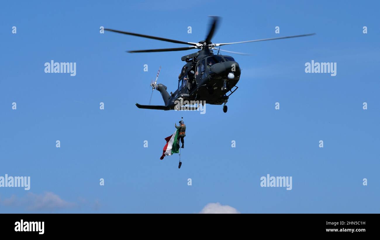Thiene Italy, OCTOBER, 16, 2021 Italian flag flying hanging from the winch of a military helicopter in flight. AgustaWestland AW139 Leonardo HH139 of Stock Photo