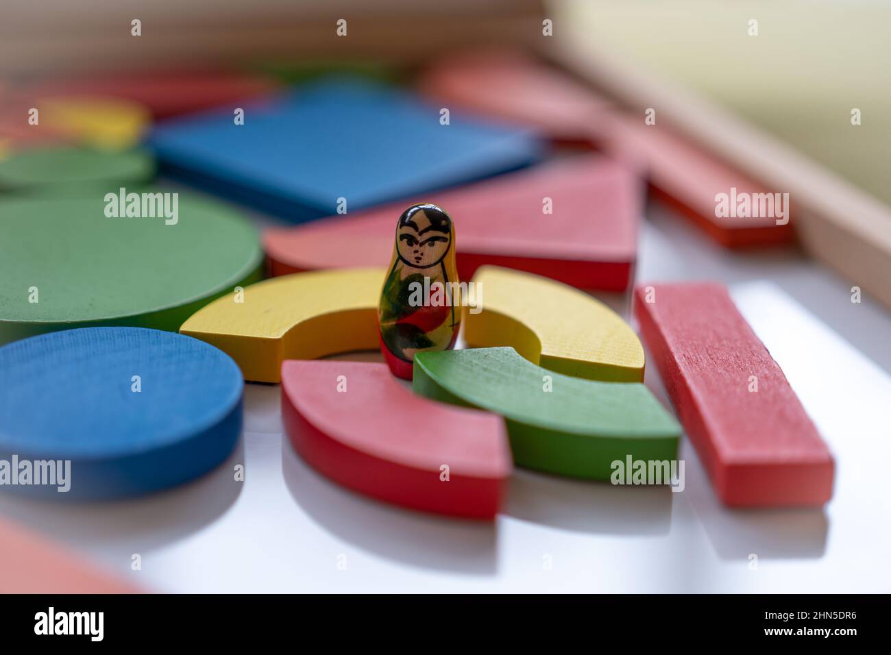 Challenging situation. Smallest Russian doll surrounded by brightly coloured wooden blocks in a tray. Stock Photo