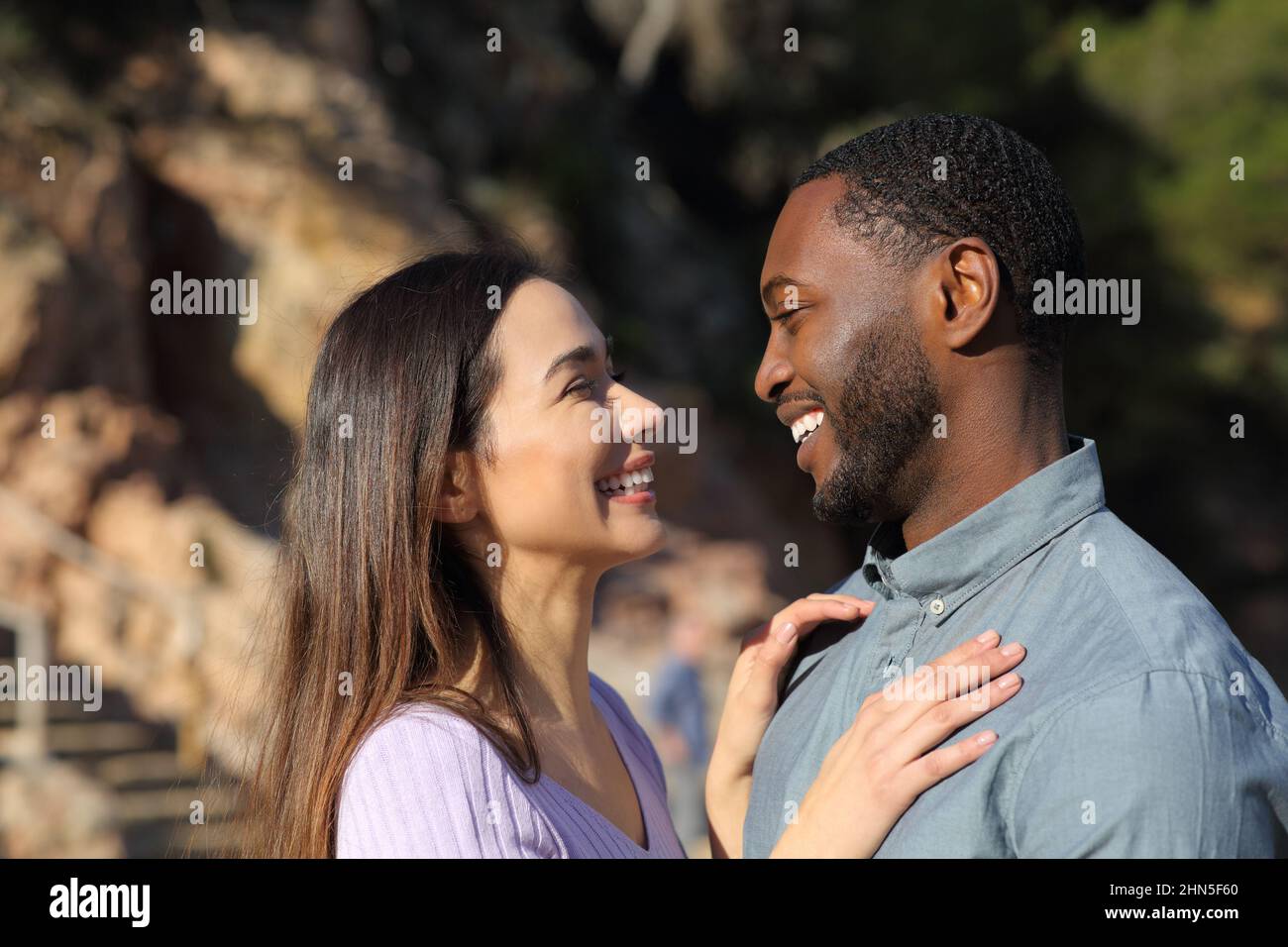 Profile of a happy interracial couple flirting falling in love looking each other Stock Photo