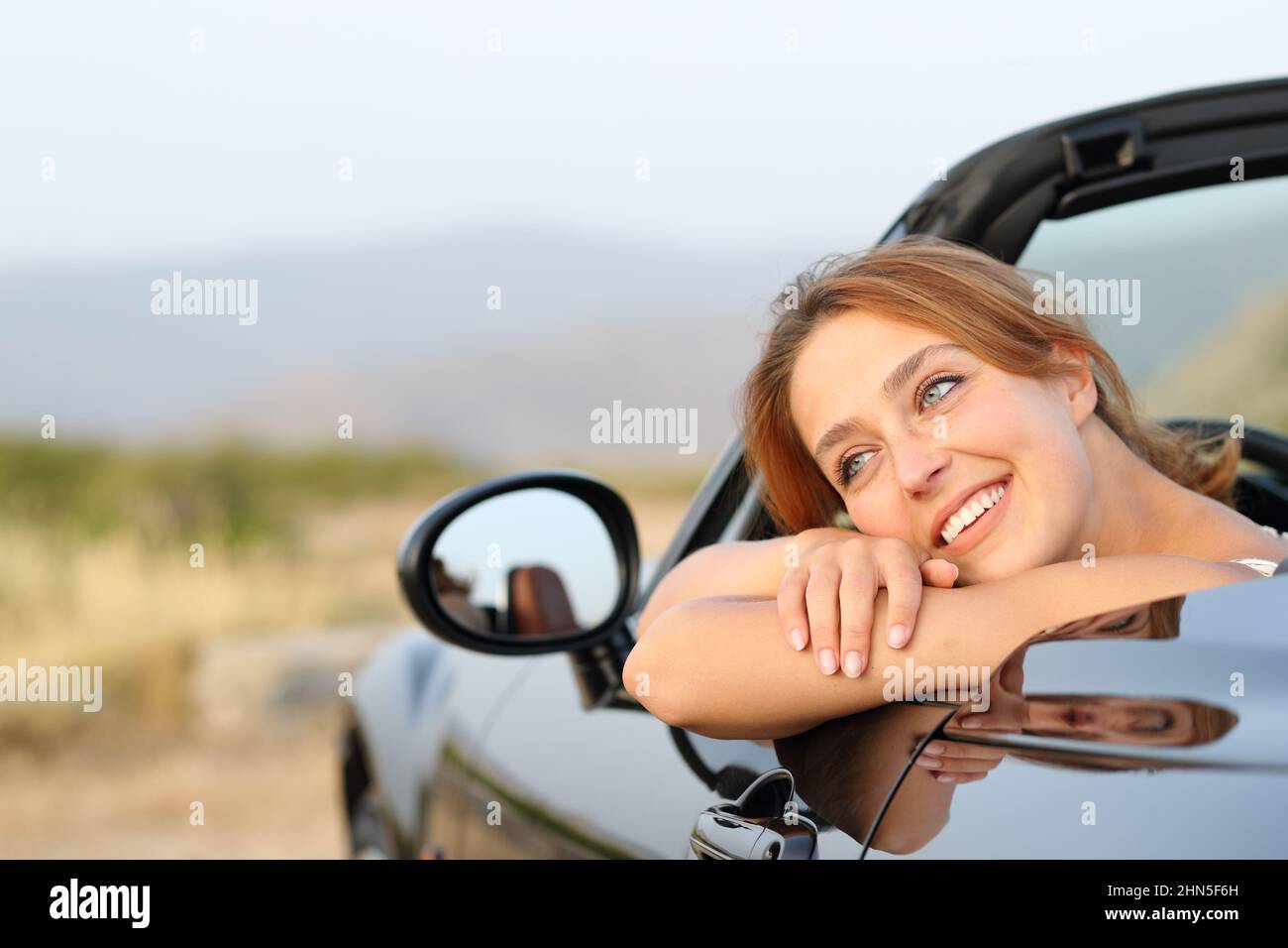 Happy owner resting sitting in a convertible car looking away in the