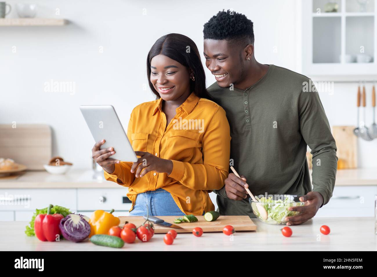 Happy Black Spouses Using Digital Tablet While Cooking Lunch In Kitchen Together Stock Photo