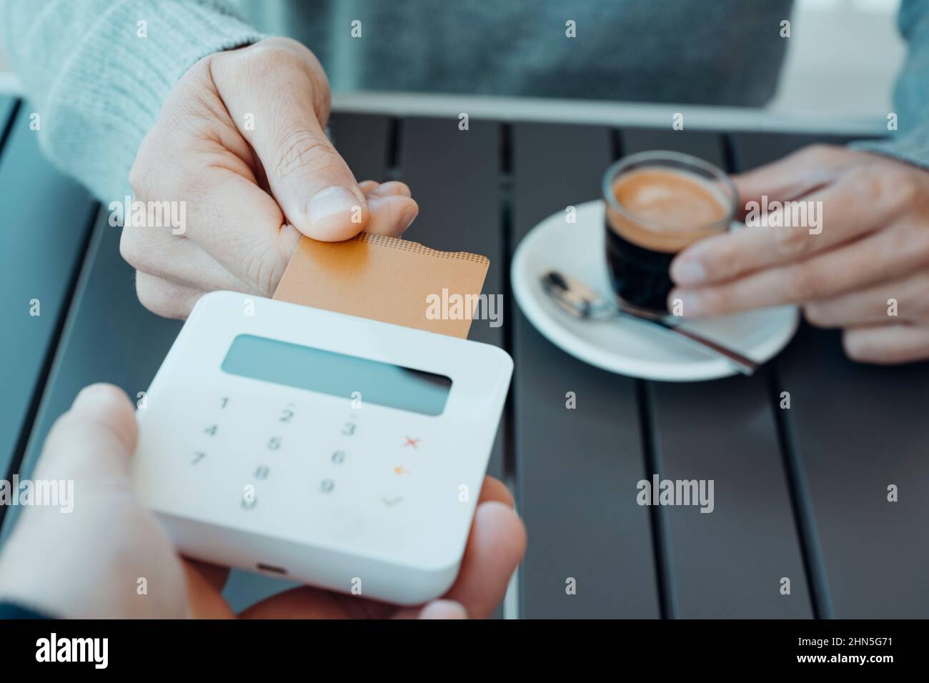 closeup of a young caucasian man, sitting on an outdoors table, about to pay the bill with his credit card, inserting it into a wireless payment termi Stock Photo