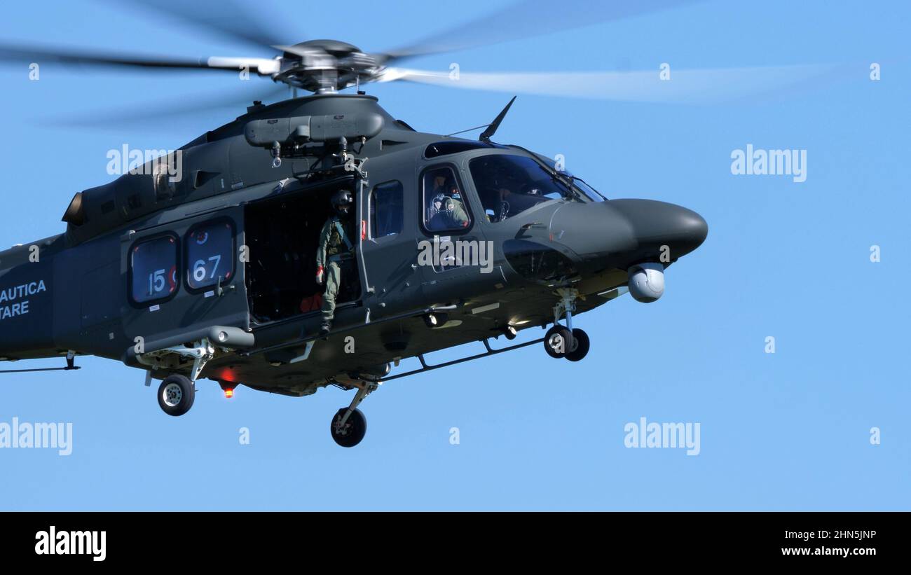 Thiene Italy, OCTOBER, 16, 2021 Dark green camouflage military helicopter flying in the blue sky with the side hatch open. AgustaWestland AW139 Leonar Stock Photo