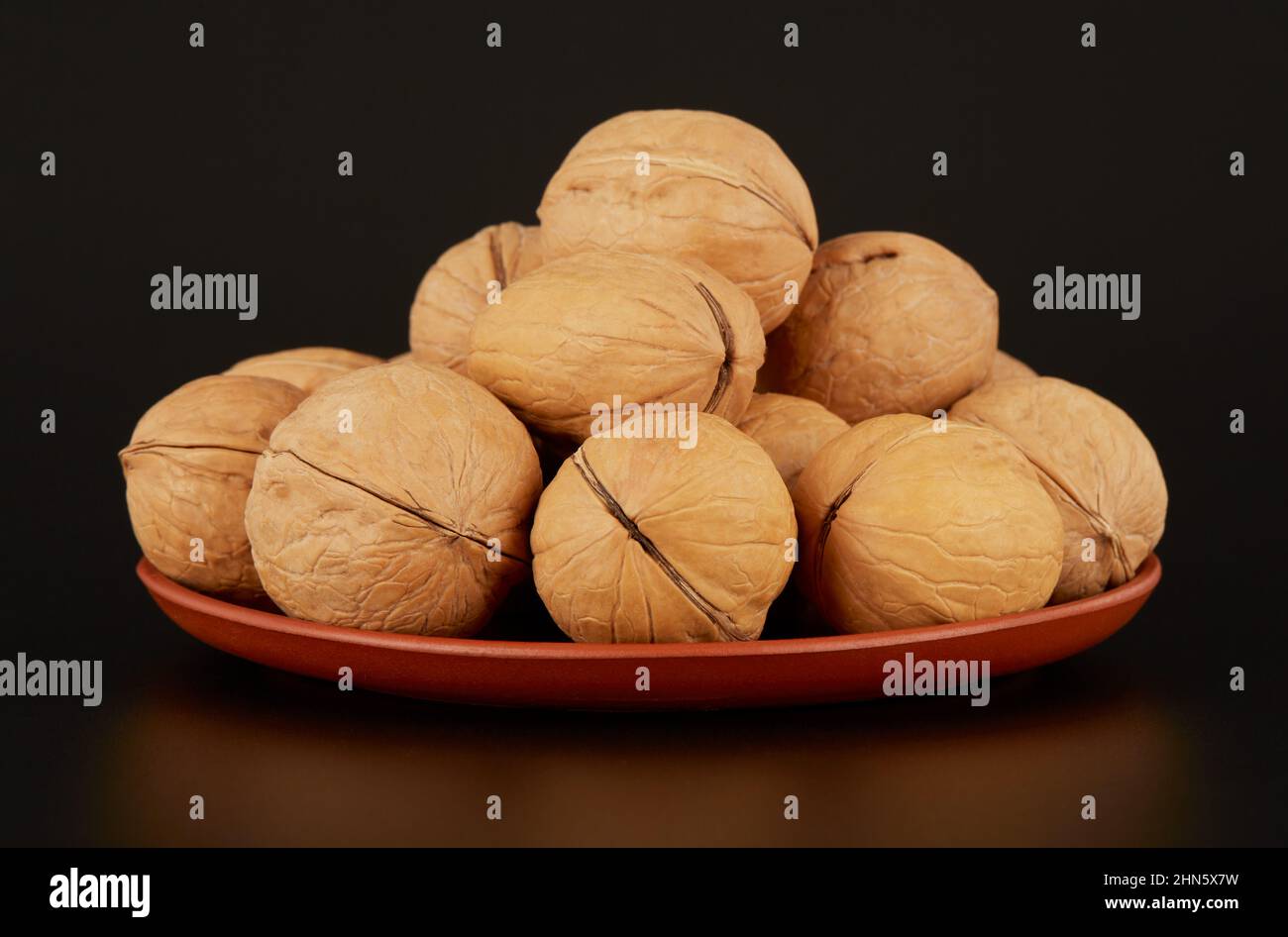 A mound of walnuts on a clay plate on a black background Stock Photo