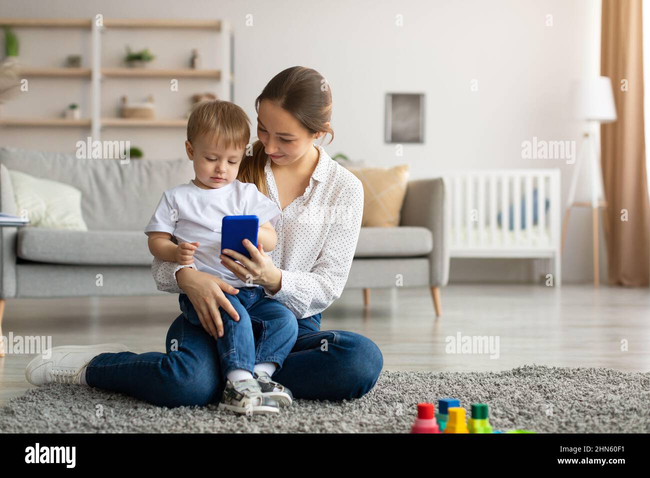 Online shopping. Young mom and her toddler son using smartphone at home ...
