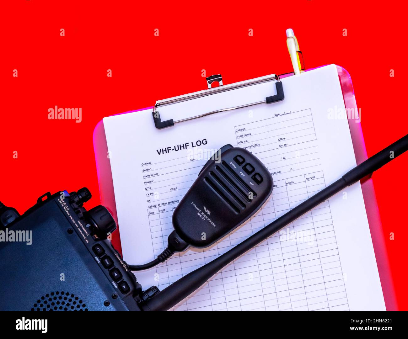 Amateur radio transceiver with antenna and microphone pictured together with a VHF/UHF radio contest log sheet clipped to a board. Stock Photo