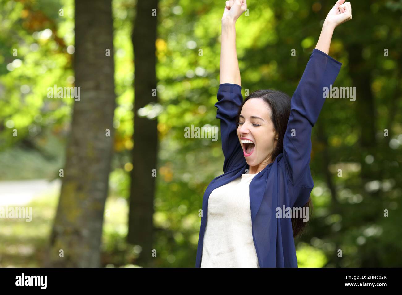 Excited woman in a park raising arms celebrating success Stock Photo