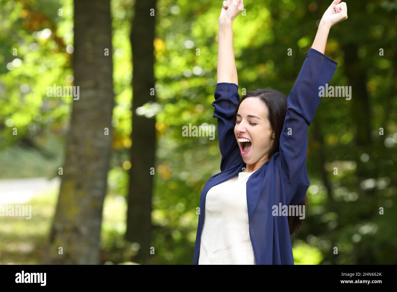 Excited woman in a park raising arms celebrating success Stock Photo ...