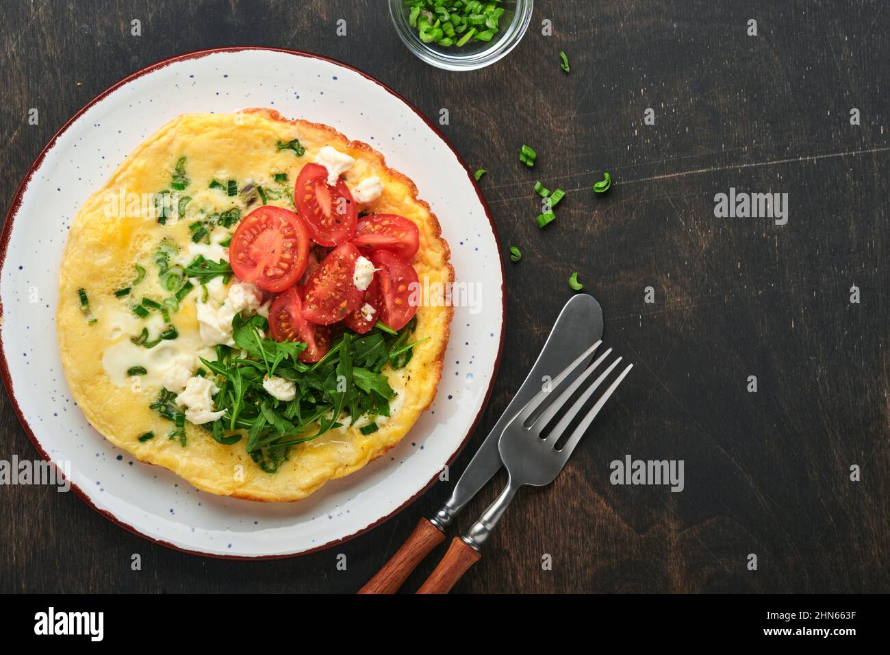 Rustic omelette or frittatas with green onions, cheese mozzarella, green arugula and tomatoes on old wooden dark background. Healthy food concept. Bre Stock Photo