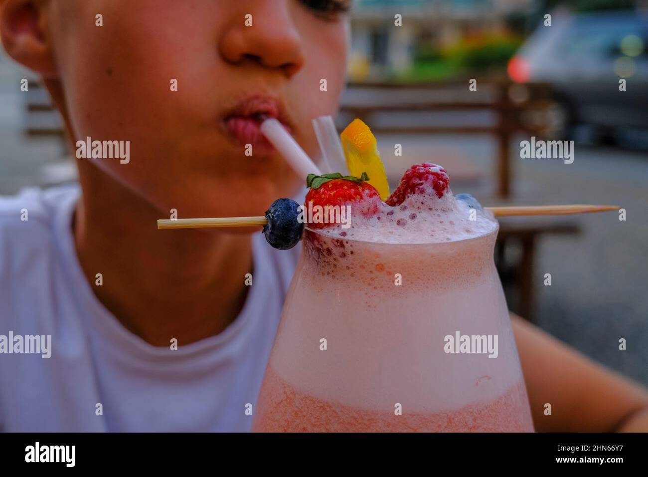kid drinking strawberry smoothie with a straw and different berries as a decor close-up. Healthy food. Healthy lifestyle. Stock Photo