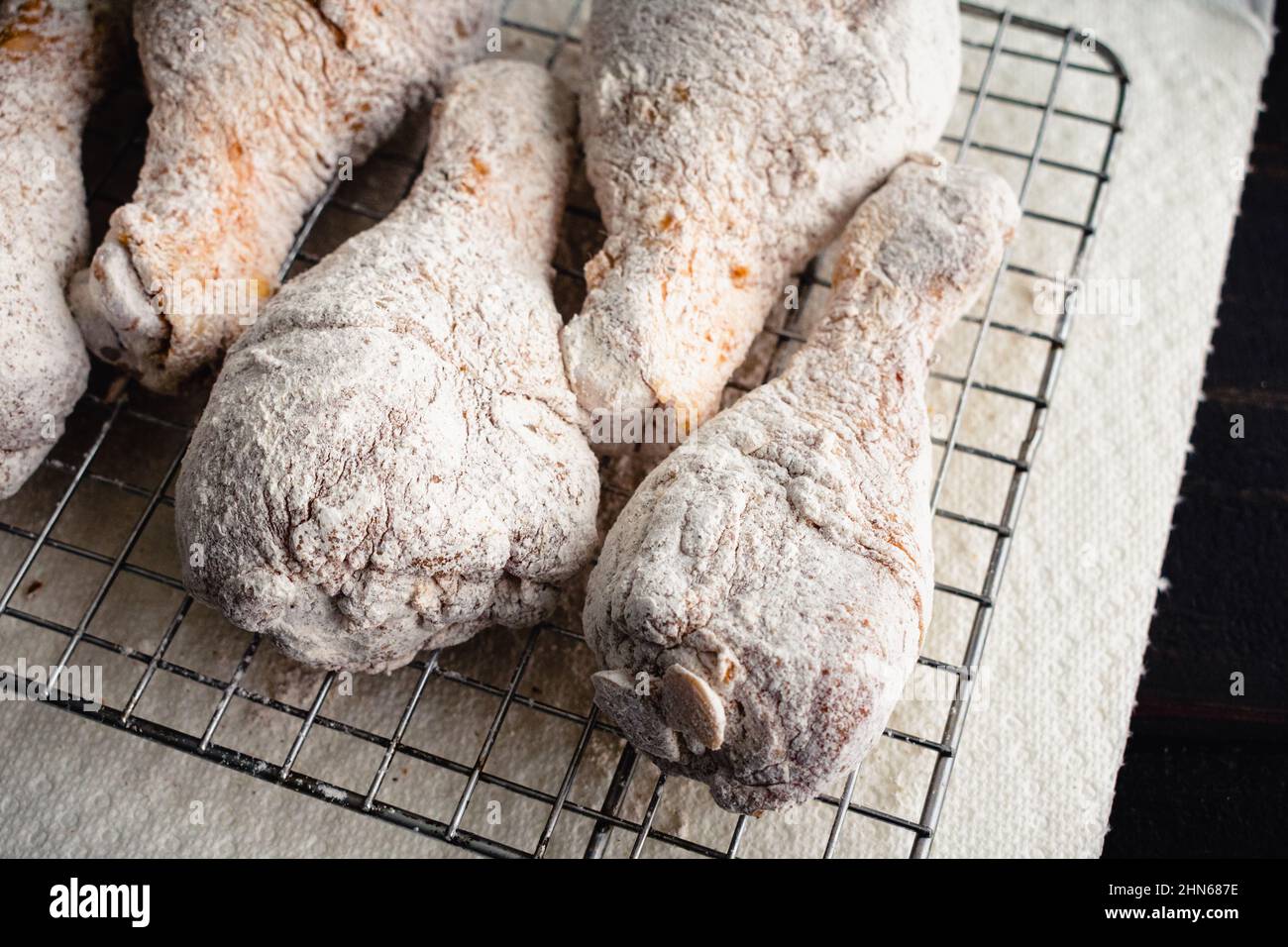Raw Floured and Spiced Chicken Drumsticks on a Wire Rack: Floured uncooked chicken legs being prepped for frying Stock Photo