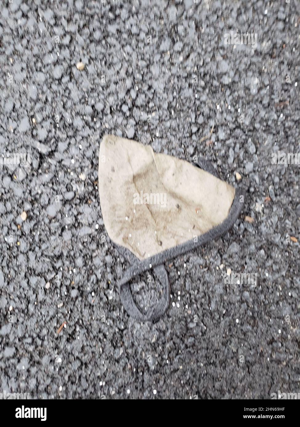 Dirty, discarded face mask on the ground Stock Photo