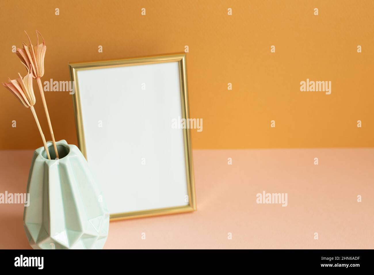 Blank photo frame with vase of dry flowers on pink table. orange wall background. copy space Stock Photo