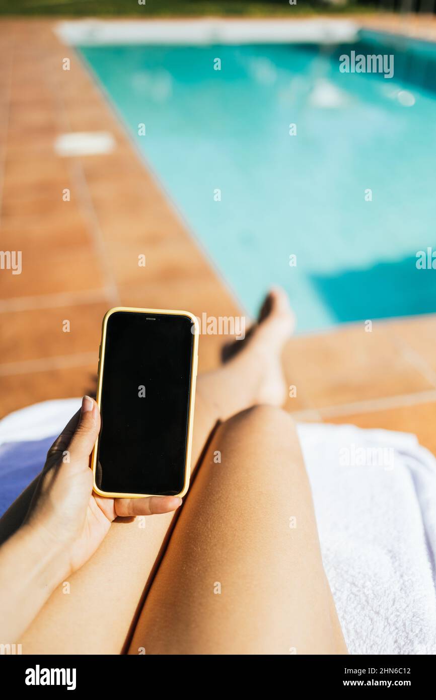 Unrecognizable woman using a smart phone while sunbathing in a swimming pool Stock Photo