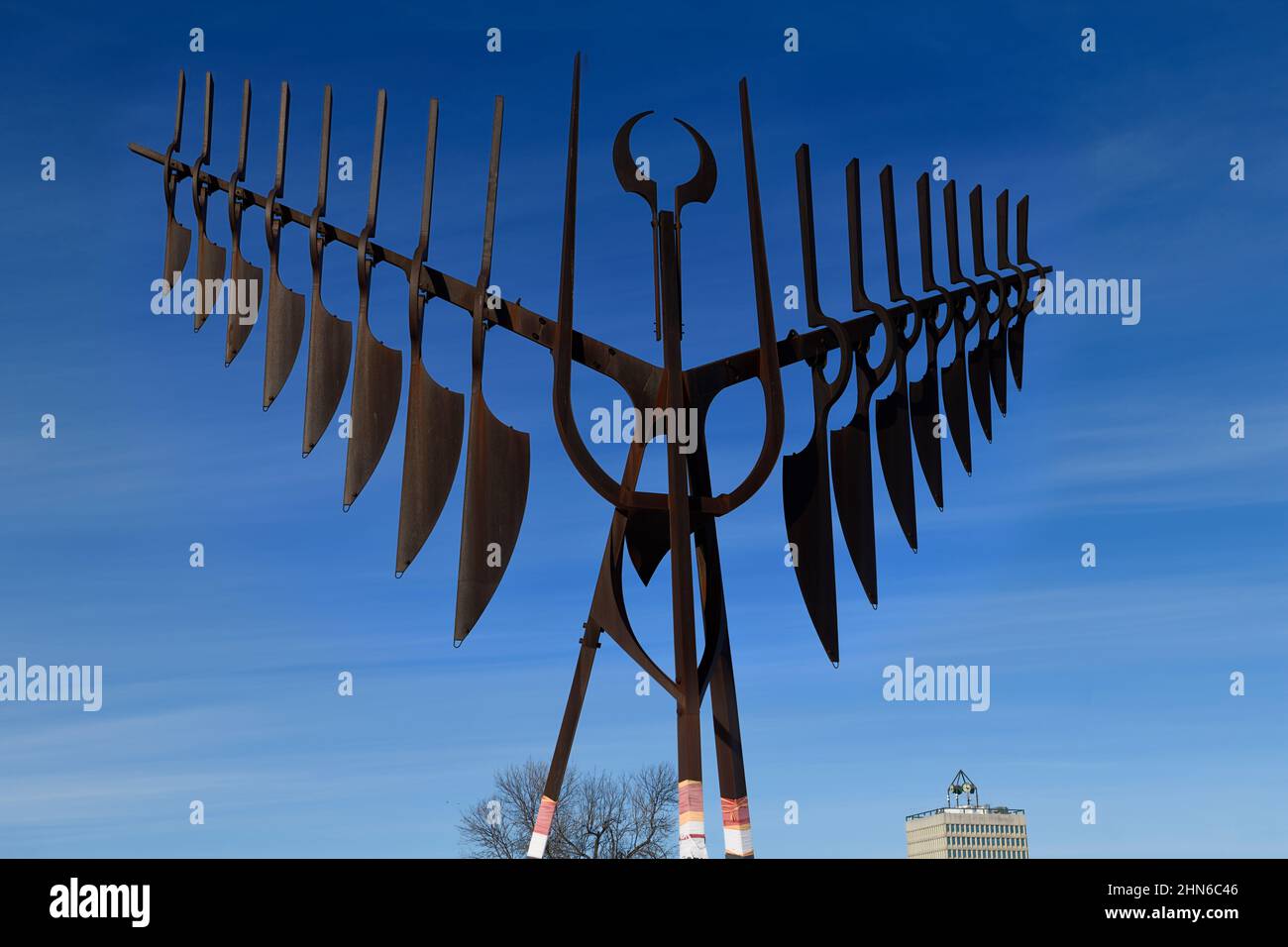 Rusted steel Spirit Catcher with Thunderbird wings with Barrie City Hall municipality office tower at Heritage Park against a blue sky Stock Photo