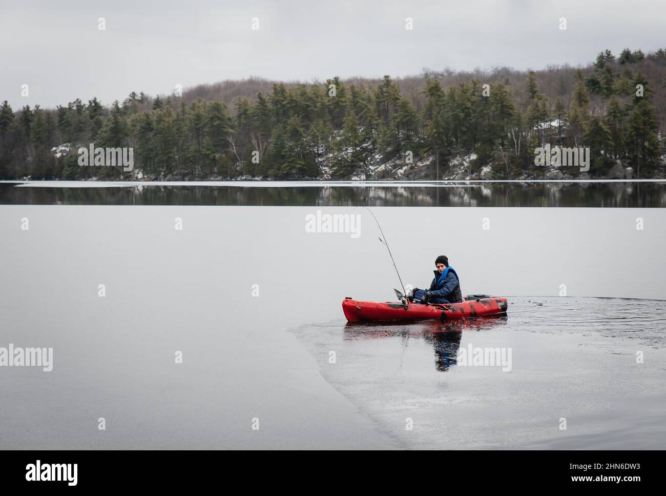 Teen boy sitting in a fishing kayak on an icy lake in winter Stock