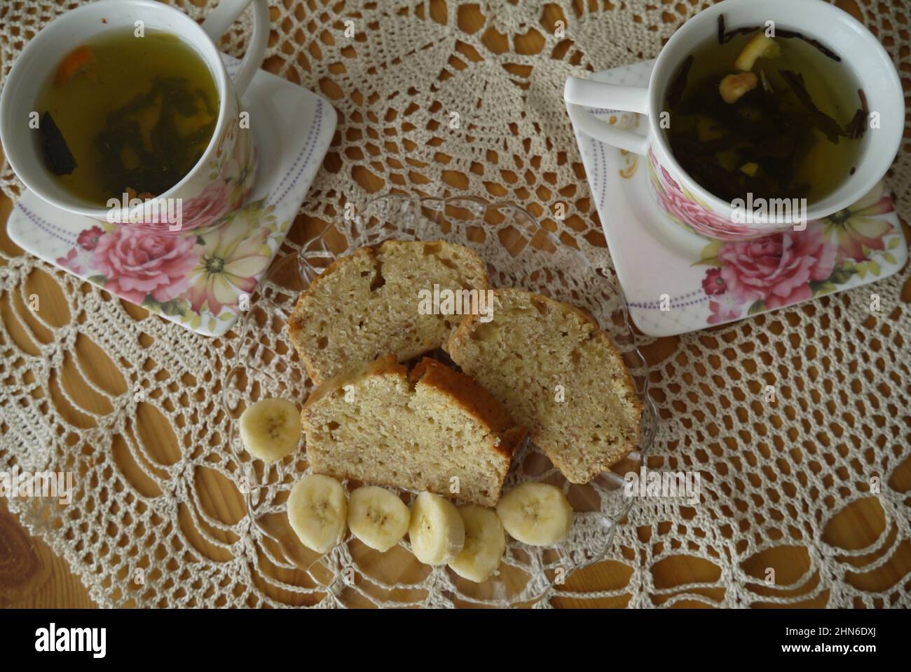 Banana bread and tea in flower cups on rustical table. Stock Photo