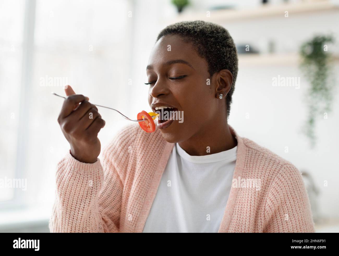 Satisfied young black woman in casual with closed eyes enjoy delicious organic salad, eat piece of vegetable Stock Photo
