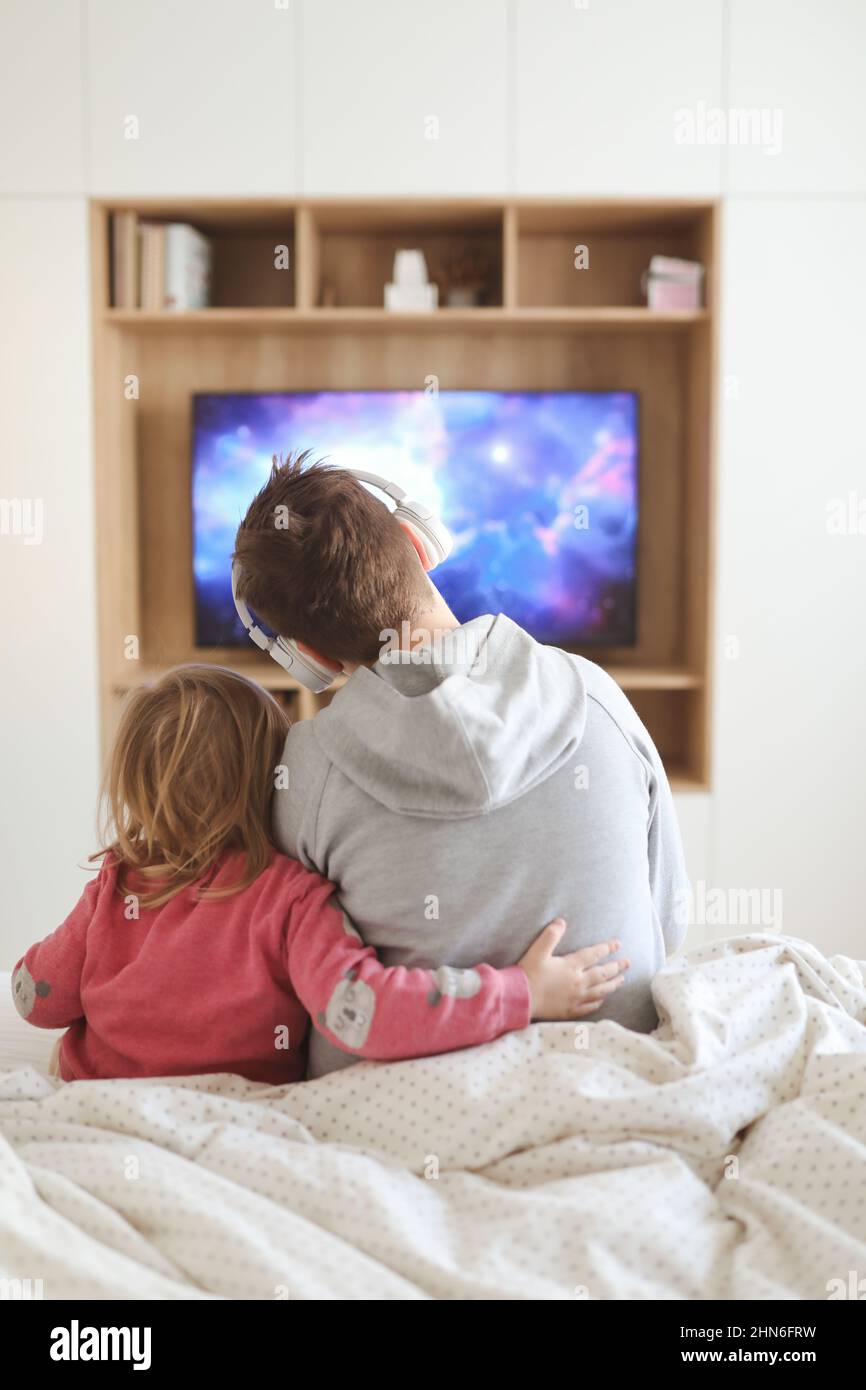 Brother and his little sister watching television, children playing video game at home. Stock Photo