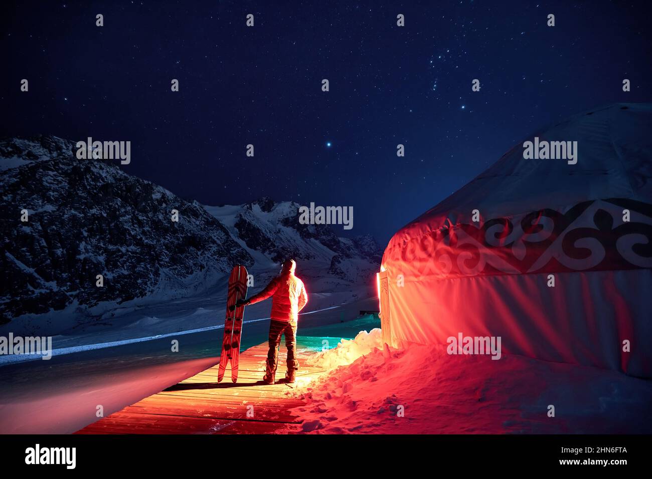 A man with a snowboard standing near a yurt at night in winter in the mountains Stock Photo