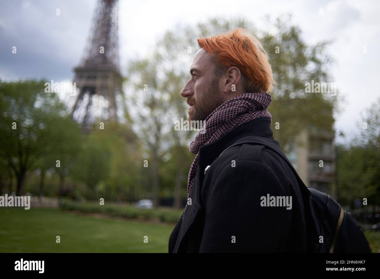 Man with dyed orange hair walking near the Eiffel Tower in Paris Stock Photo