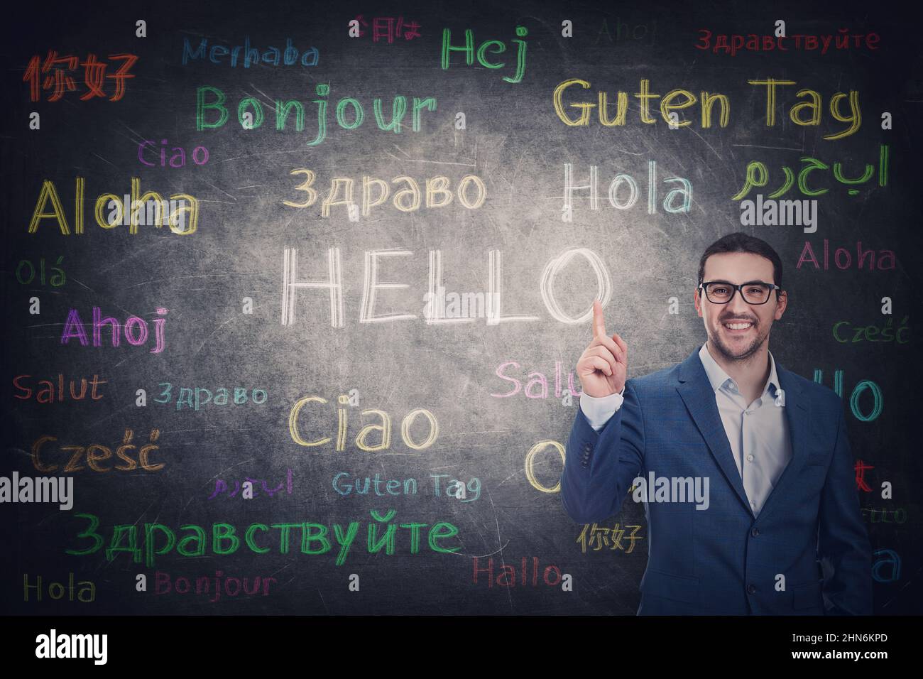 Confident businessman knows different languages. Person shows index finger to the blackboard with word hello translated in multiple foreign languages. Stock Photo