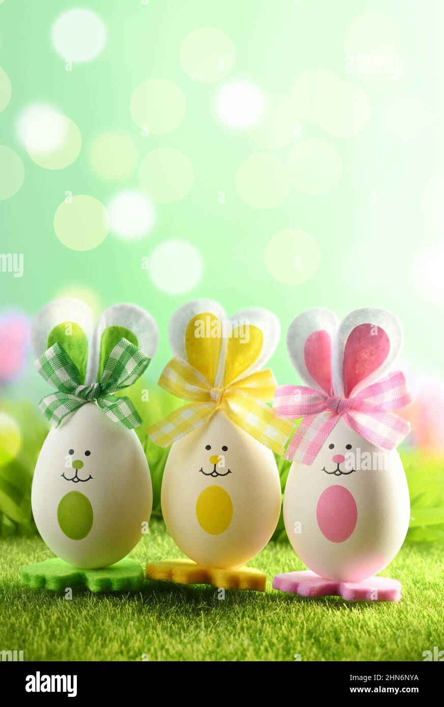 Funny easter eggs in the grass on blurred background. Happy Easter background. Easter compositions with cute rabbits eggs. Stock Photo