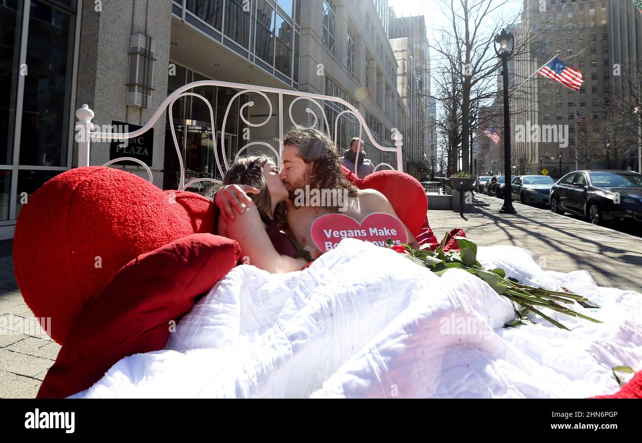 Raleigh, North Carolina, USA. 14th Feb, 2022. SKY DAWSON, l, of Fort Wayne, IN and LUIS CORREAL of Atlanta, GA share a kiss while they cuddle in a bed in the heart of Downtown Raleigh, NC with a message saying ''˜Vegans Make Better Lovers.' People for the Ethical Treatment of Animals set up the display in downtown choosing Valentine's Day to remind everyone eager to please their partners that the cholesterol in meat and dairy can clog the arteries to all your organs, not just the heart. (Credit Image: © Bob Karp/ZUMA Press Wire) Stock Photo