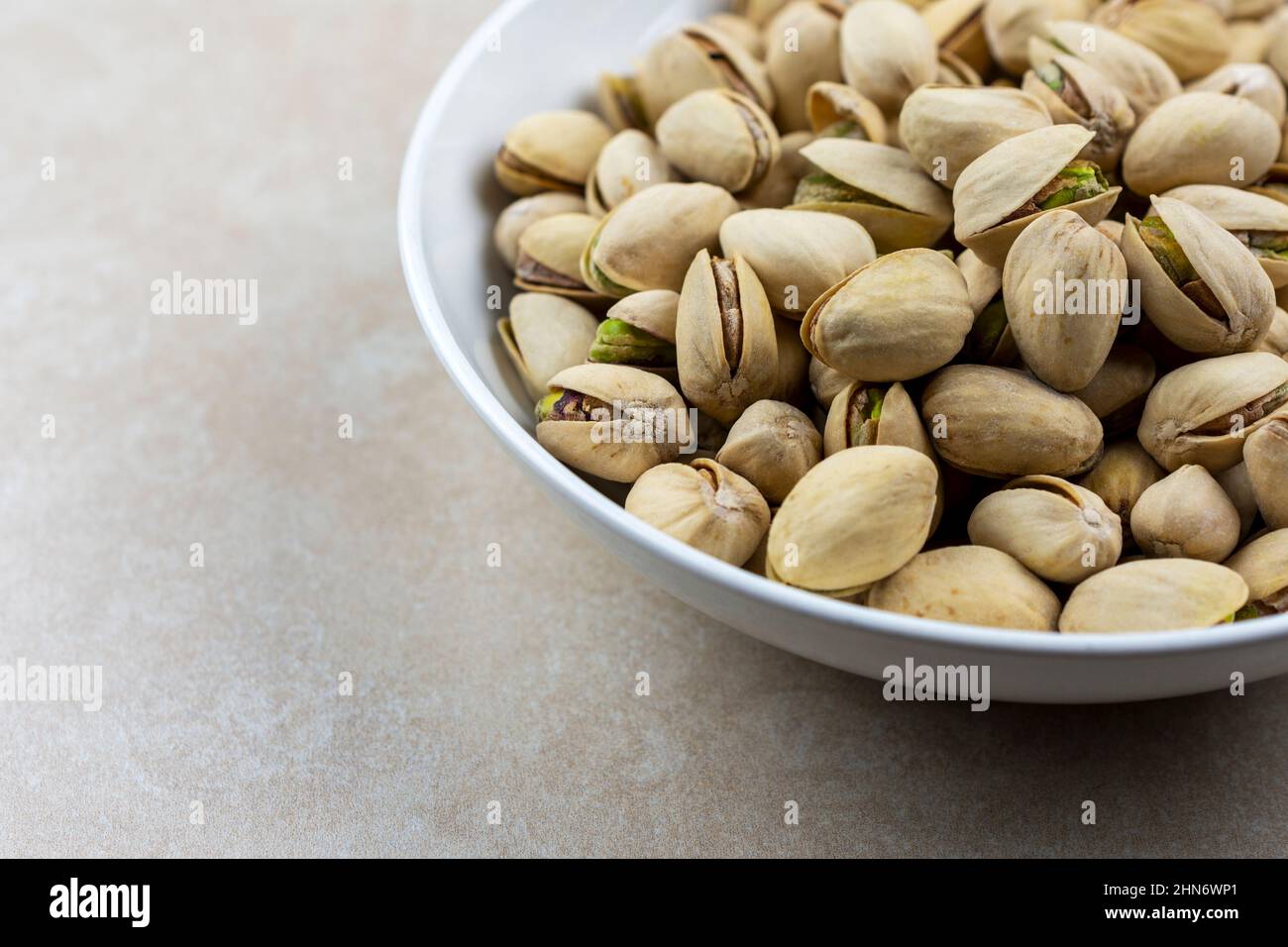 Side view of a white bowl of pistachios on a tile surface. Stock Photo