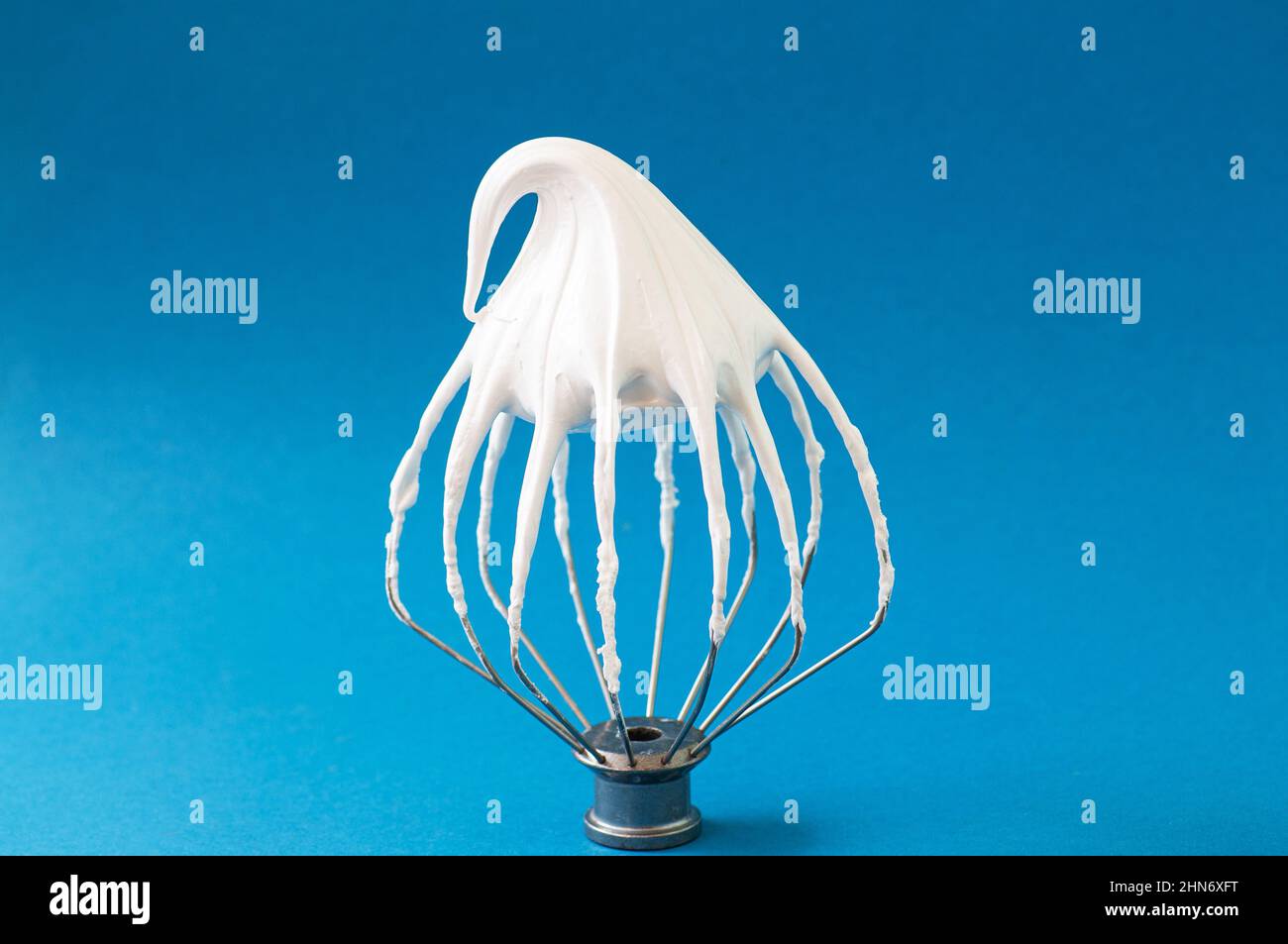Whipped egg whites - beaten italian meringue on a wire whisk on blue background,  closeup and copy space. Stock Photo