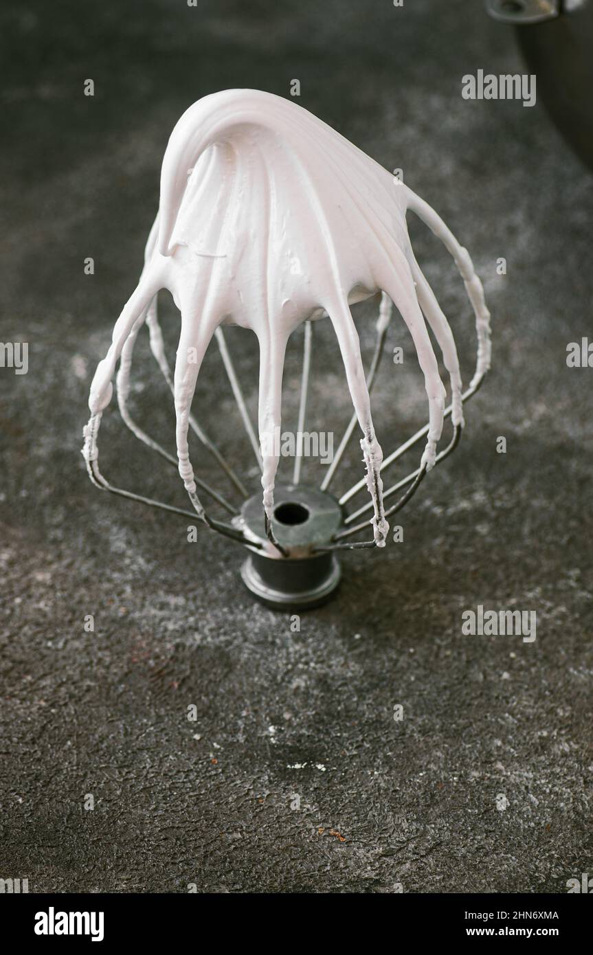 Whipped egg whites beaten italian meringue on a wire whisk on gray