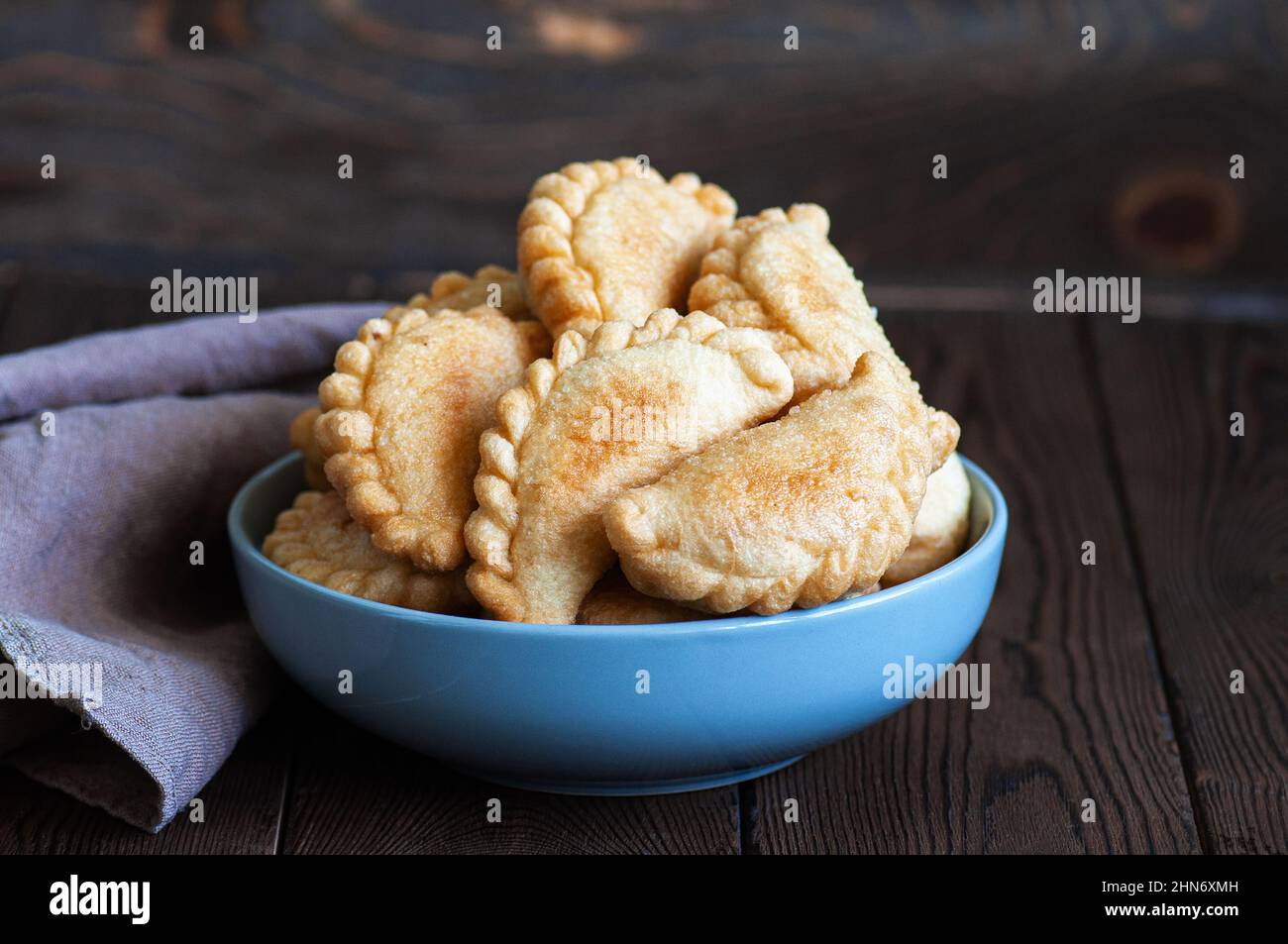 Freshly fried hand pies with meat in a bowl on a wooden background. Close up. Stock Photo
