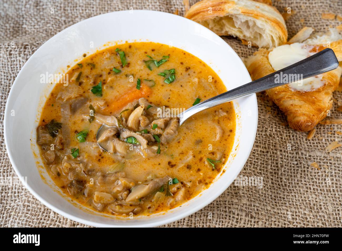 Healthy oyster mushroom soup, croissant with butter on jute background