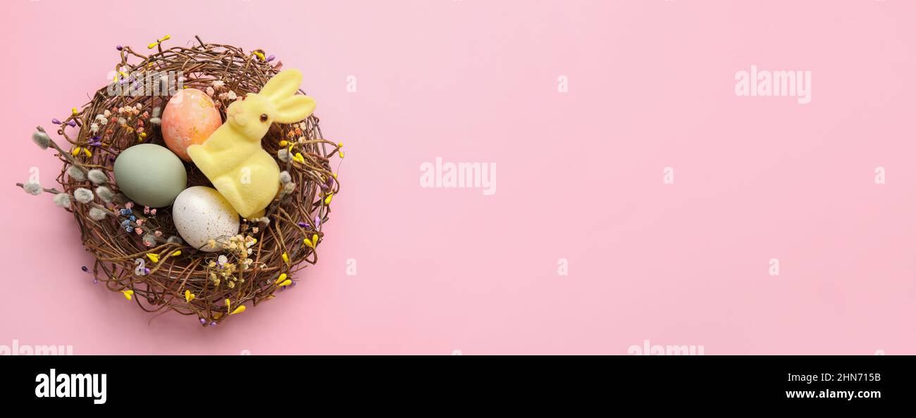 Nest with painted Easter eggs and bunny on pink background with space ...