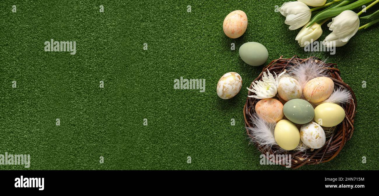 Nest with painted Easter eggs and tulips on green background with space ...