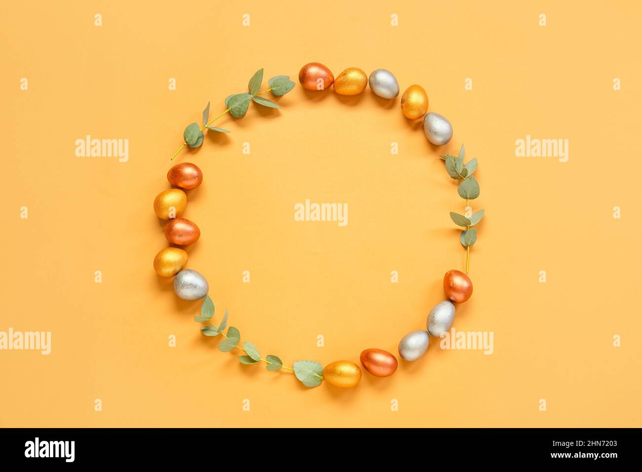 Frame made of Easter eggs and eucalyptus branches on orange background Stock Photo