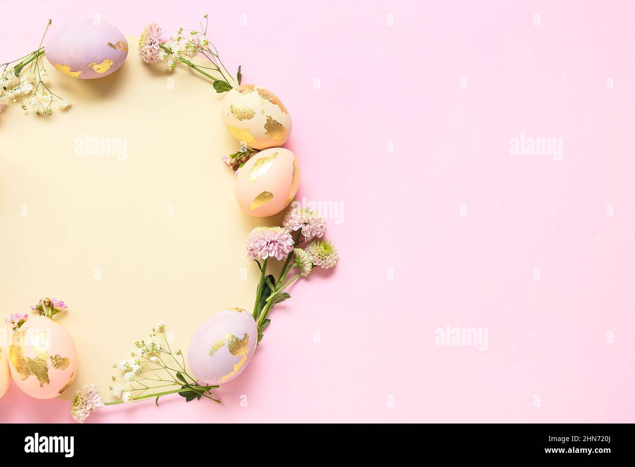 Frame made of Easter eggs, flowers and sheet of paper on pink ...