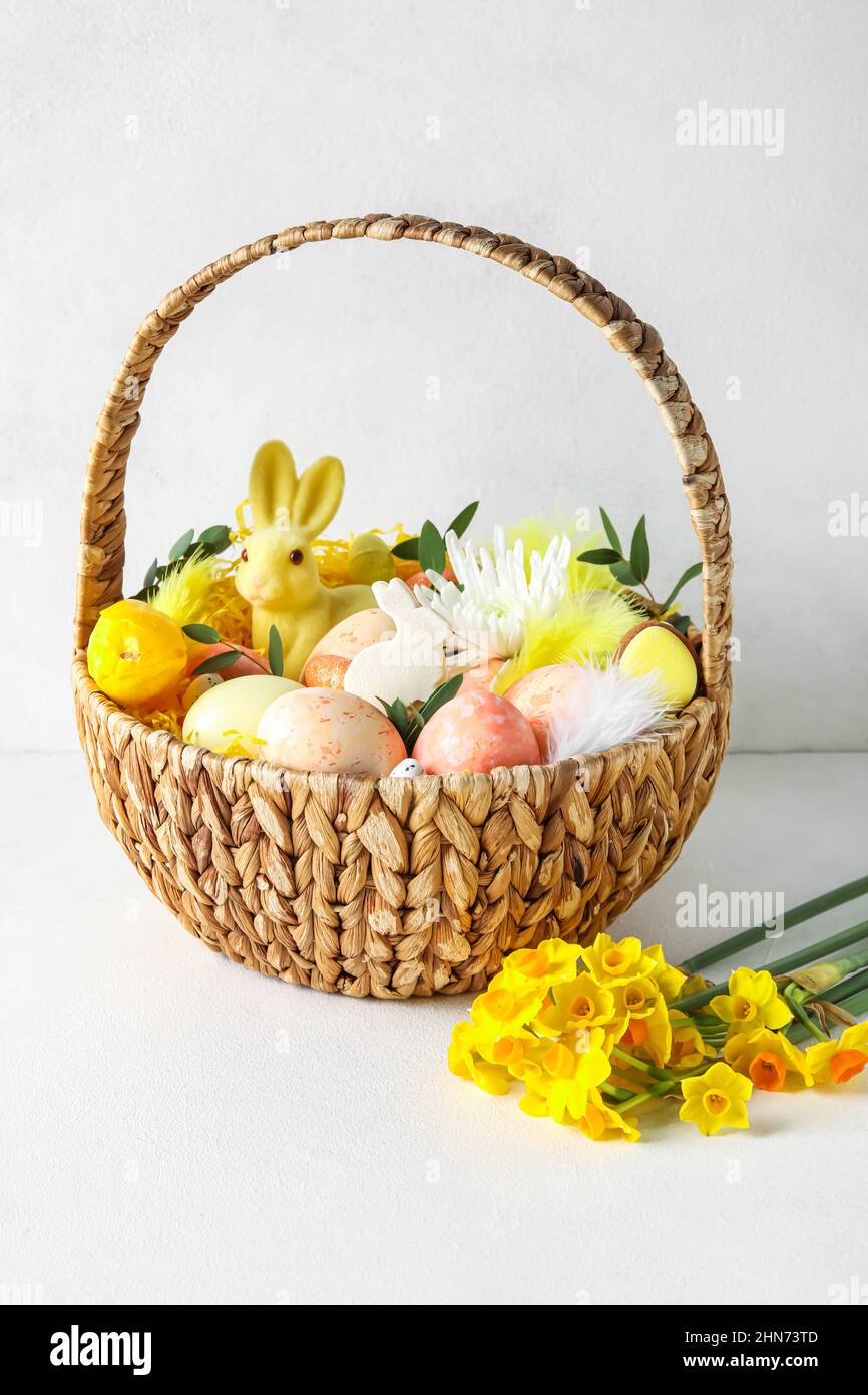 Basket with painted Easter eggs, bunny and flowers on light background ...