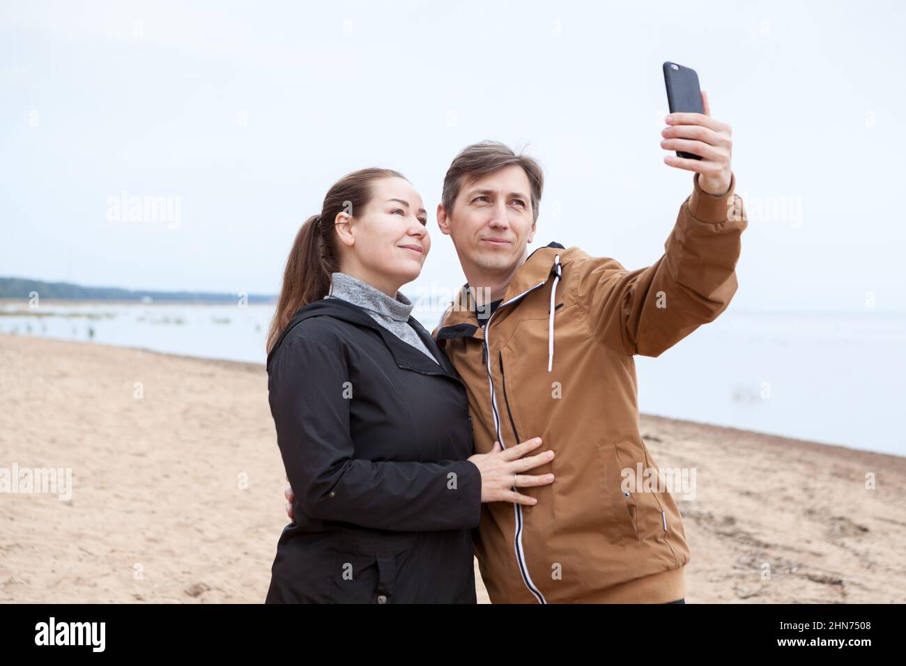 Loving couple taking selfie while walking on coastline, Caucasian people Stock Photo