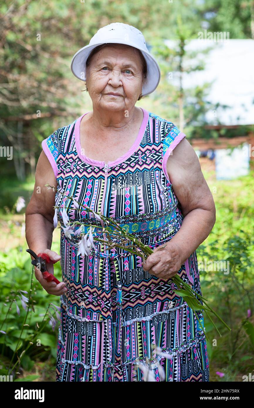 Gardening woman cutting her flowers in garden, old lady works with averruncator, portrait at spring season Stock Photo