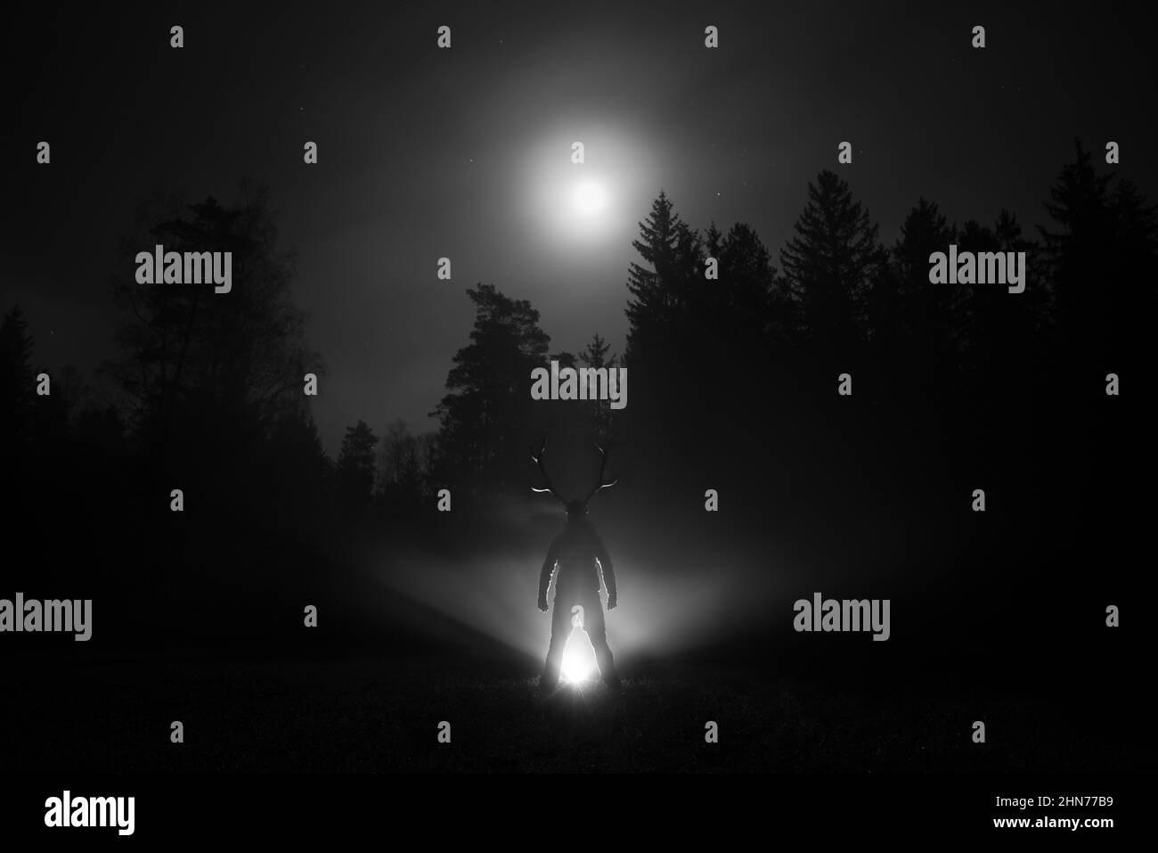 Person wearing a scary costume posing in a forest in grayscale Stock Photo