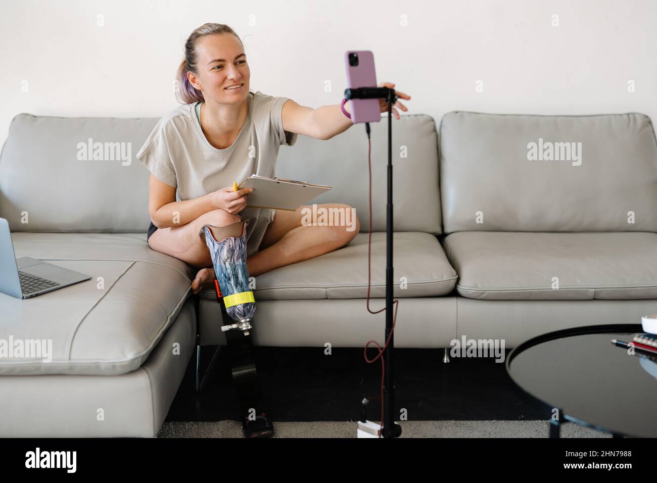 Smiling Young Woman With Prosthetic Leg Using Laptop In Living