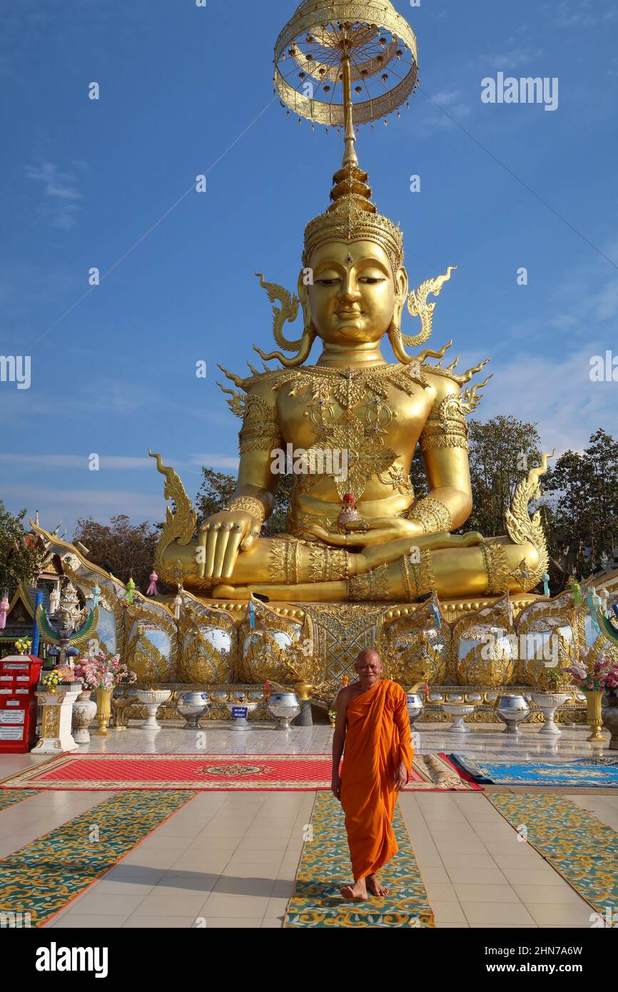 Golden statue of buddha  with smiling Buddhist  monk walking in front. Wat Phra That Doi Saket, Chiang Mai, Thailand. Stock Photo