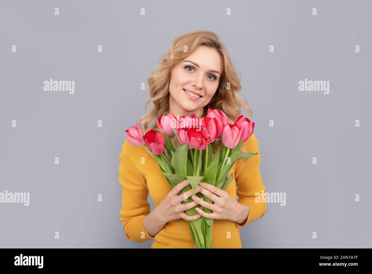 smiling lady hold flowers for spring holiday on grey background Stock Photo