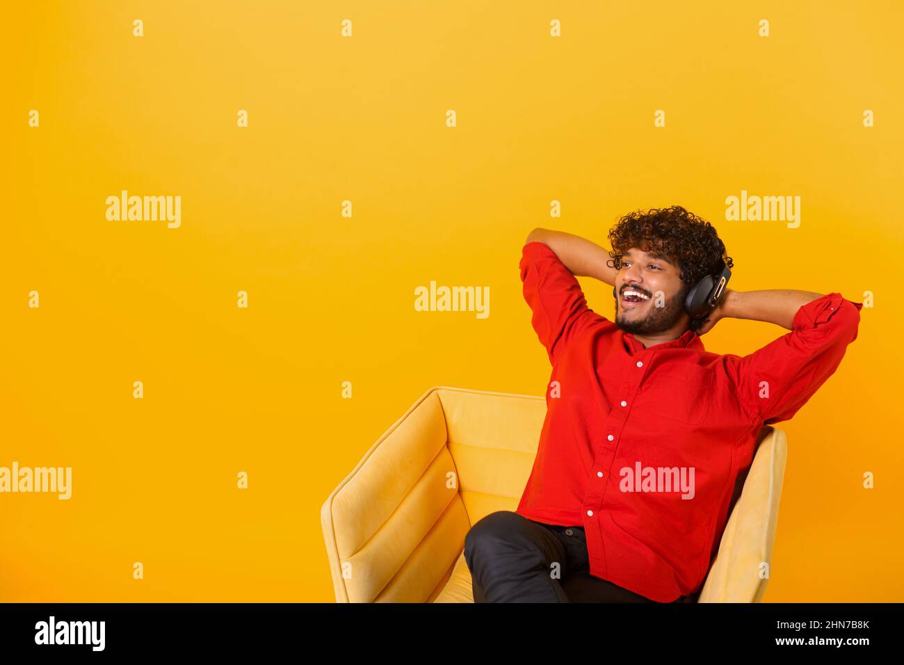 Studio portrait of relaxed cheerful indian man wearing and holding wireless headphones isolated on orange wall, enjoying listening to favorite music soundtrack, wellbeing. Meditation concept Stock Photo