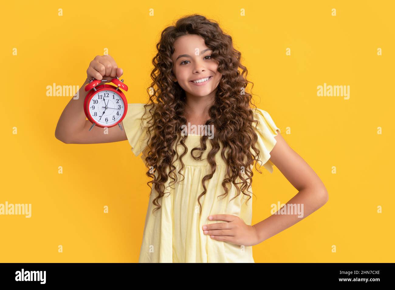 cheerful child with alarm clock. school kid curly hair showing clock. you are late. deadline. Stock Photo
