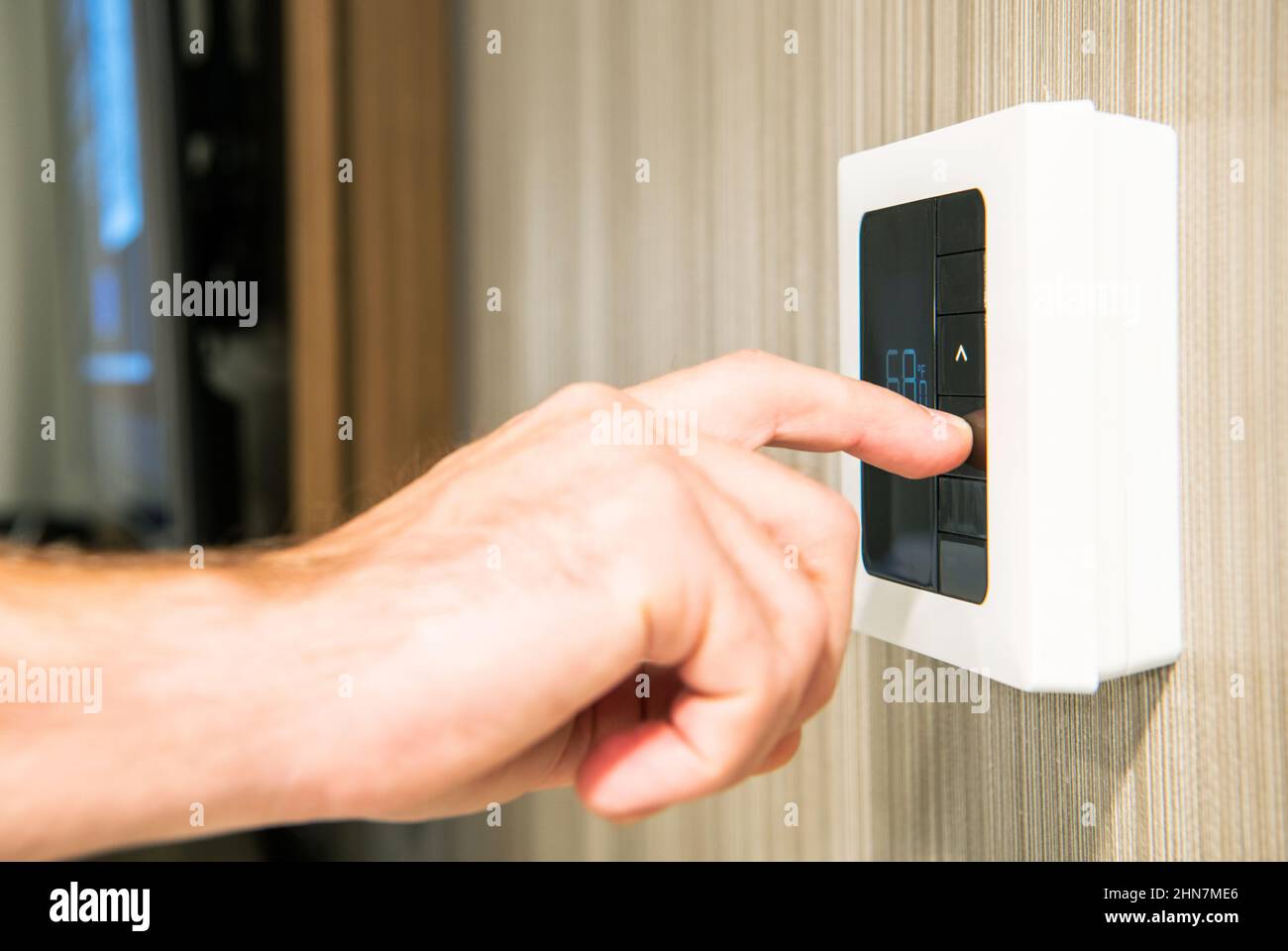 Caucasian Men Setting Residential Modern Wall Thermostat to Lower Temperature To Save Energy During Winter Time Colder Days. Stock Photo