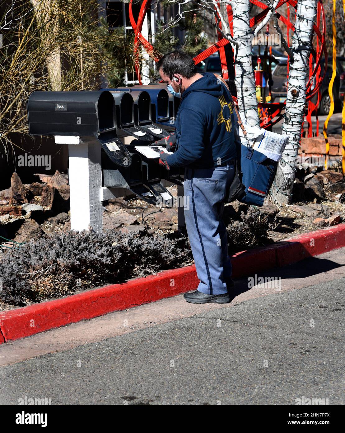 An American mailman or letter carrier delivers mail to a row of mailboxes in Santa Fe, New Mexico. Stock Photo